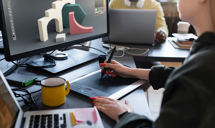 Logicmind-post-Graphic e Designer creates 3D shapes on graphics tablet as colleague works on laptop in bright workspace.